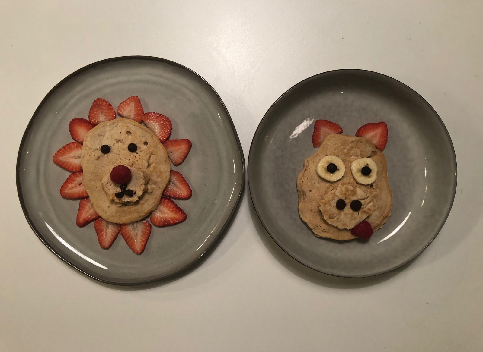 Plates with food art of a pig and lion made out of pancakes and fruit