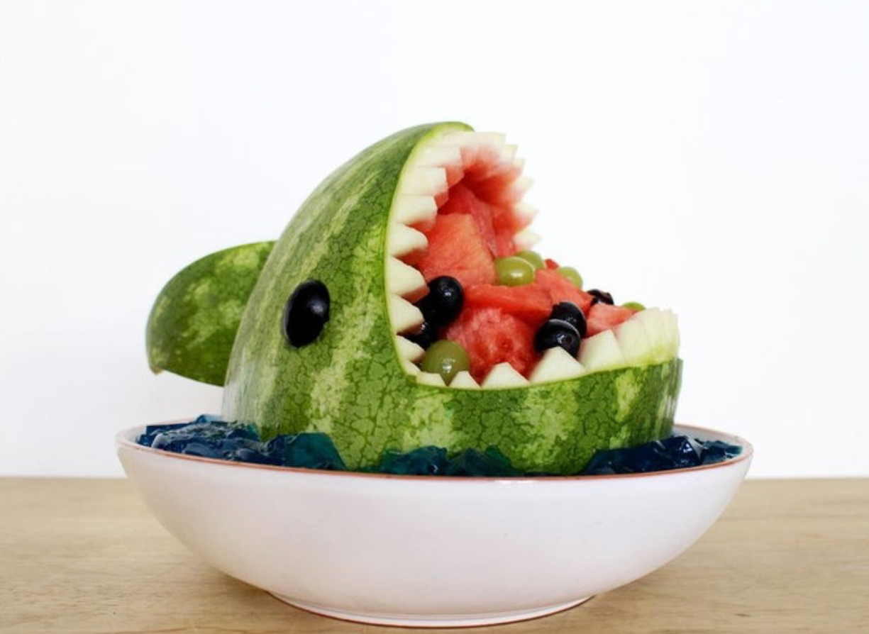 Watermelon cut into the shape of a shark with watermelon chunks and grapes in the mouth