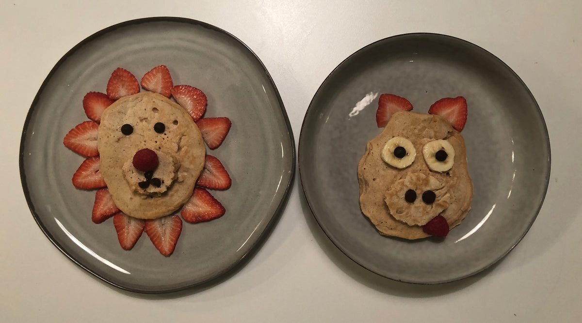 Plates with food art of a pig and lion made out of pancakes and fruit