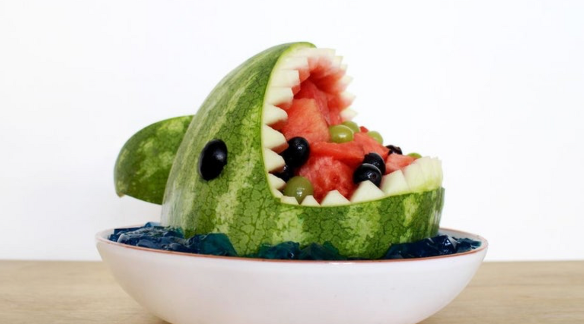Watermelon cut into the shape of a shark with watermelon chunks and grapes in the mouth